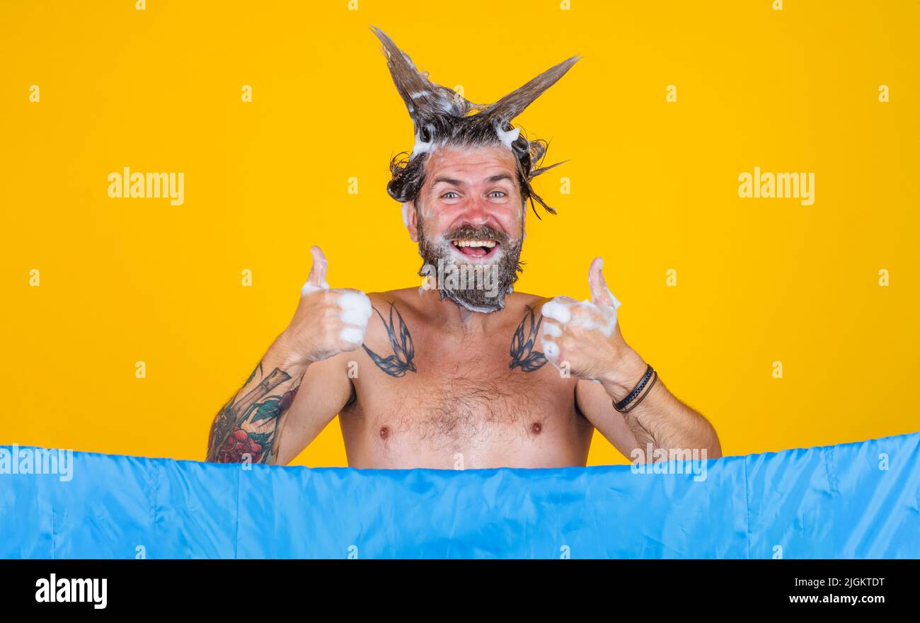Bearded man taking shower shows thumbs up. Male with foam on head. Hair care. Bathing. Showering. Stock Photo