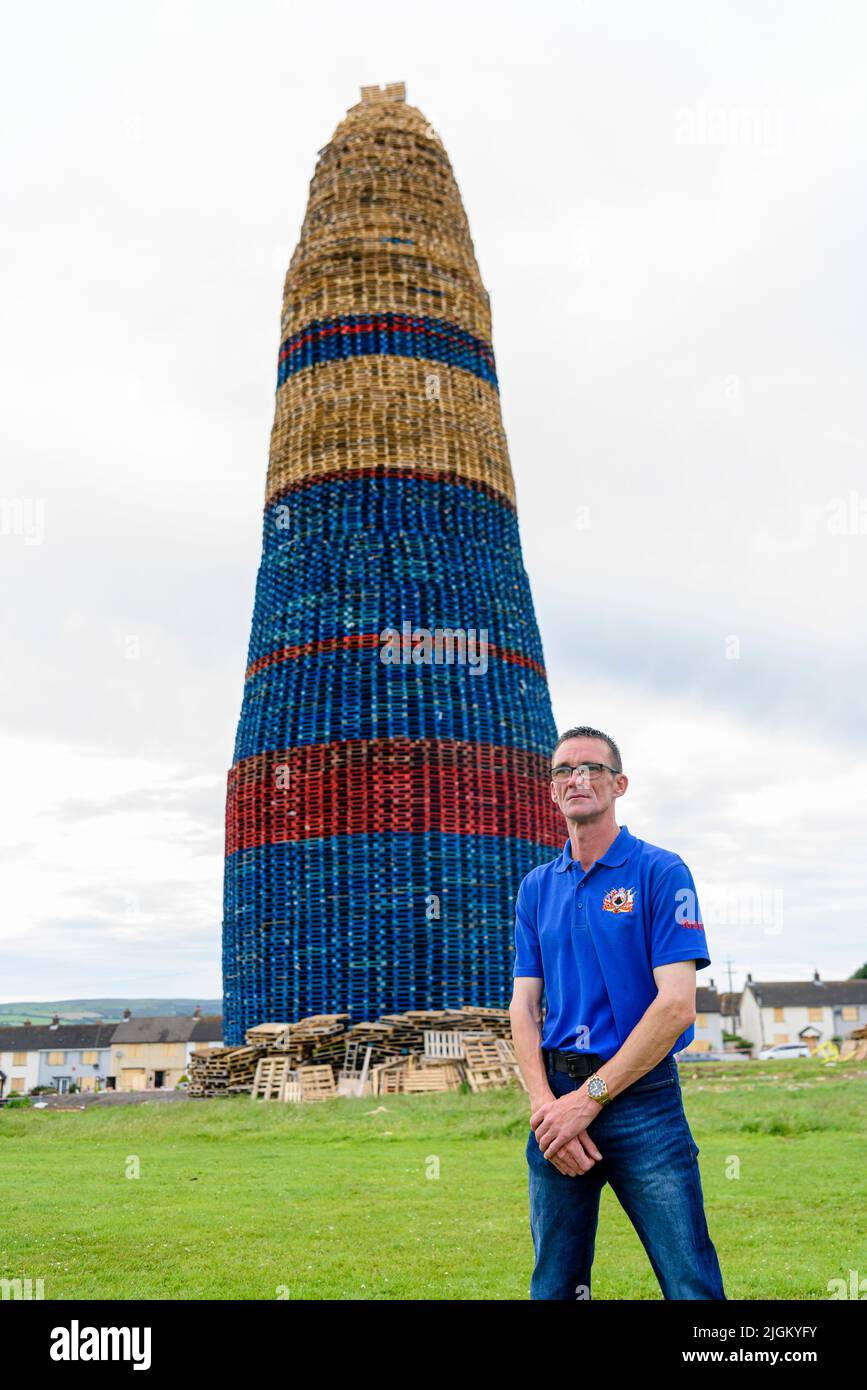 Larne, Northern Ireland, United Kingdom, UK. 11th July 2022 - Francis Hutchinson, a member of the bonfire committee, stands beside Craigyhill bonfire, which has been officially declared the world's tallest at a height of 203 feet (61.8m). Credit: Stephen Barnes/Alamy Live News Stock Photo