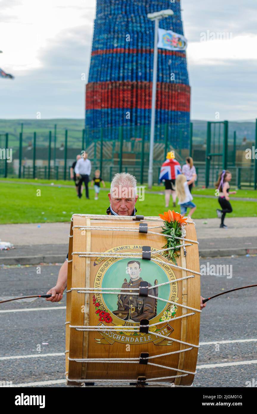 Larne, Northern Ireland, United Kingdom, UK. 11th July 2022 - A man plays a traditional lambeg drum in front of Craigyhill bonfire, which has been officially declared the world's tallest at a height of 203 feet (61.8m). Stock Photo