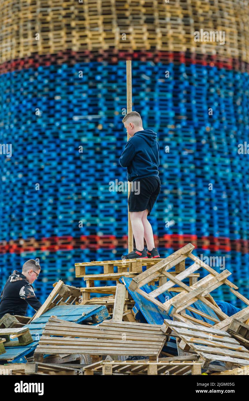 Larne, Northern Ireland, United Kingdom, UK. 11th July 2022 - Children climb onto the small bonfire beside Craigyhill bonfire, which has been officially declared the world's tallest at a height of 203 feet (61.8m). Credit: Stephen Barnes/Alamy Live News Stock Photo