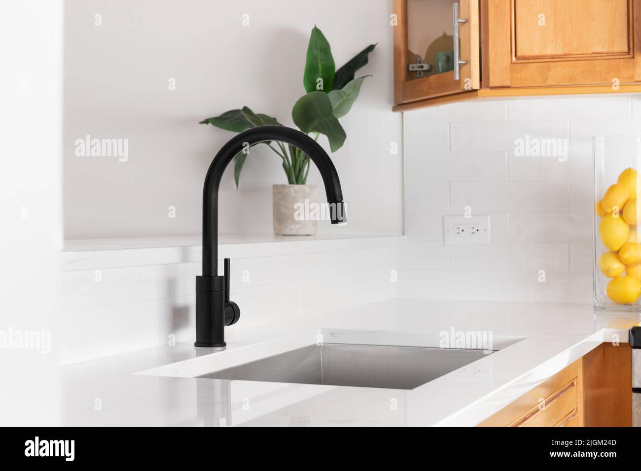 A kitchen sink detail shot with white marble countertop, black faucet, and a wood cabinets. Stock Photo