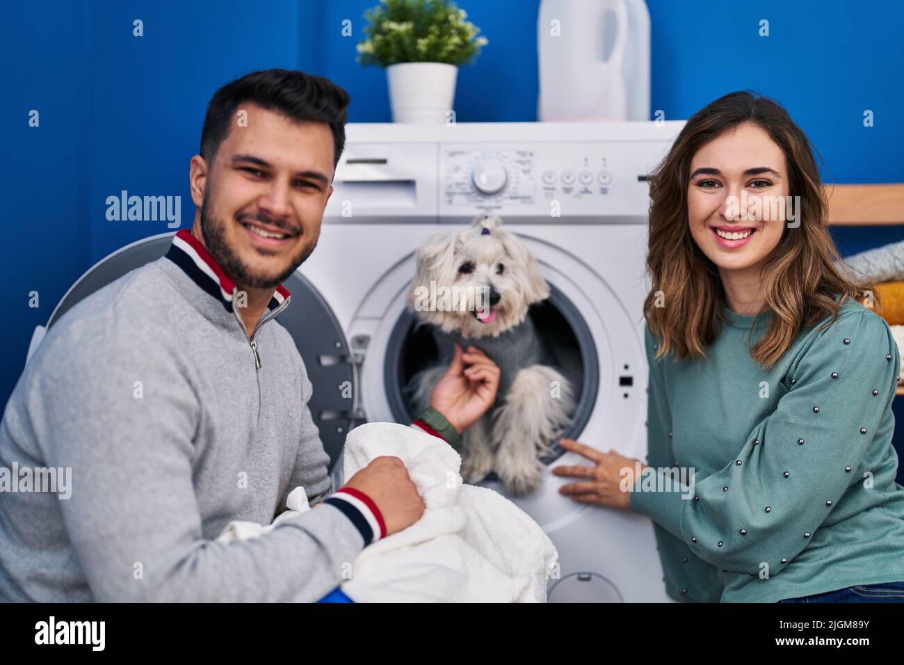 Man and woman washing clothes with dog in washing machine at laundry