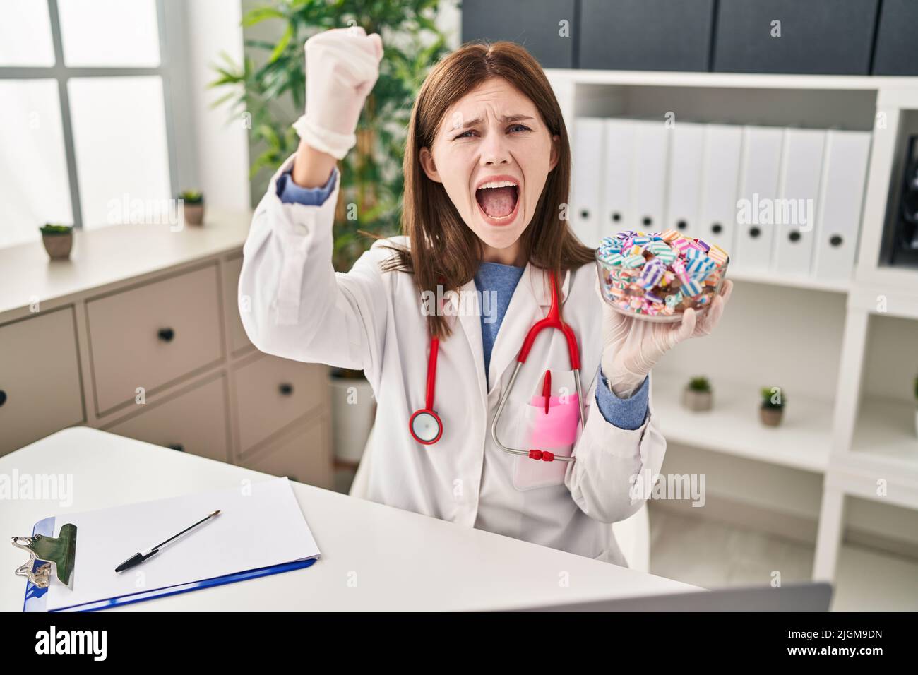 Young doctor woman holding sweets candy annoyed and frustrated shouting ...