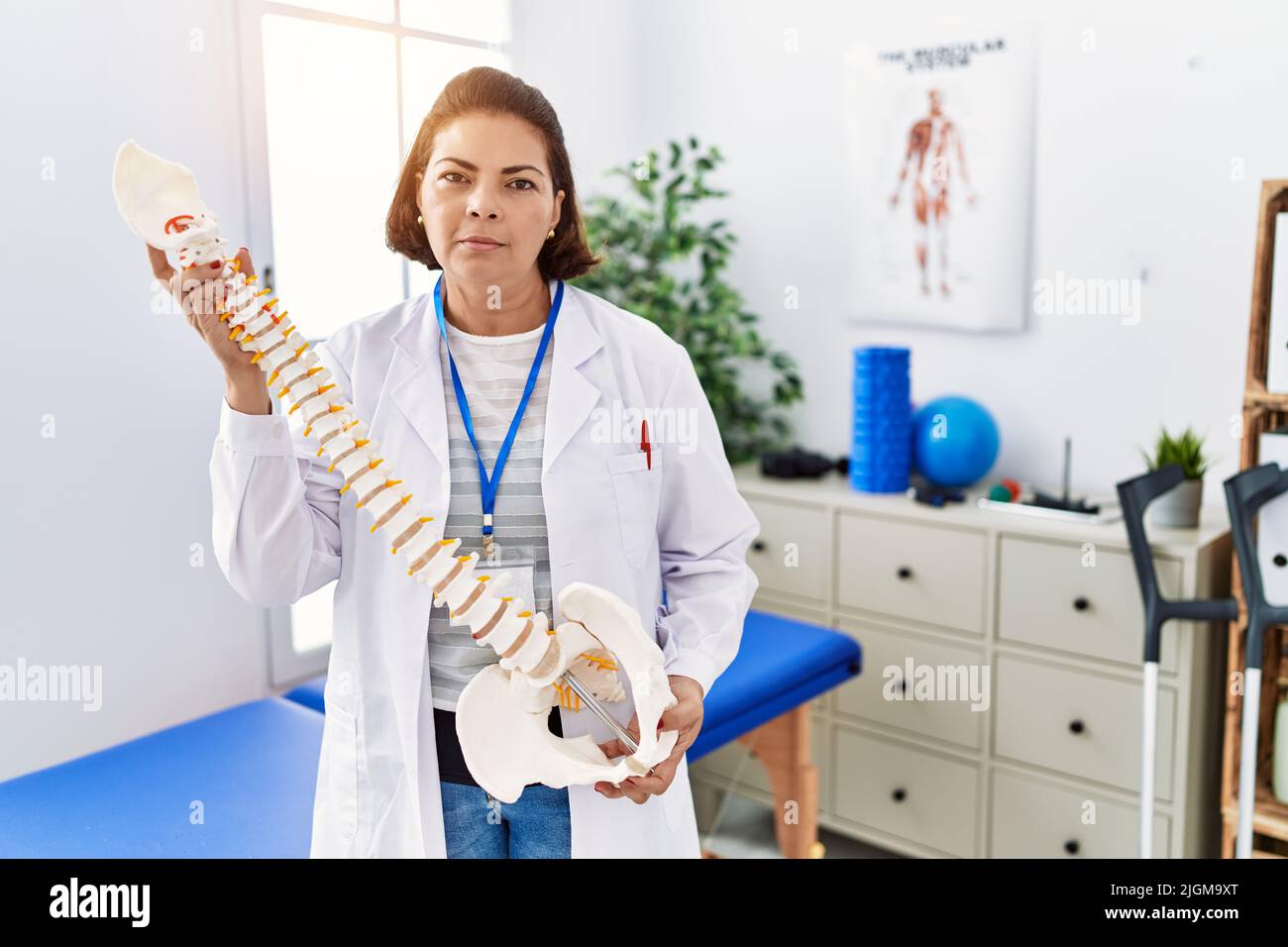 Middle age hispanic physiotherapy woman holding anatomical model of