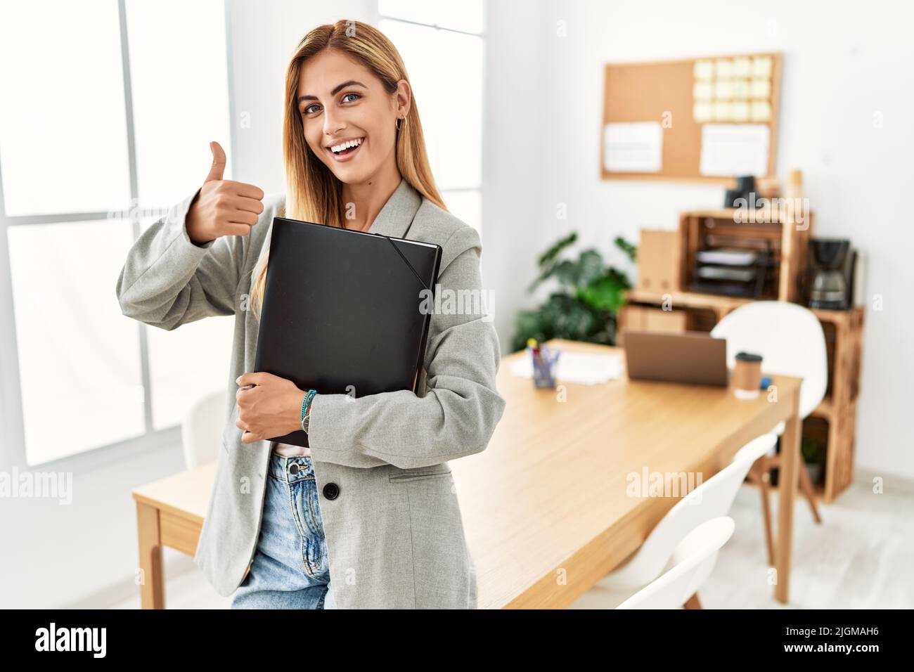 Blonde business woman at the office doing happy thumbs up gesture with ...