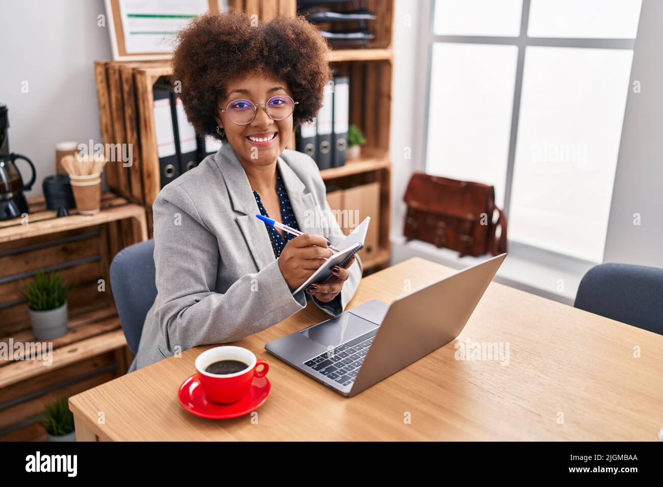 African american woman business worker using laptop writing on notebook ...