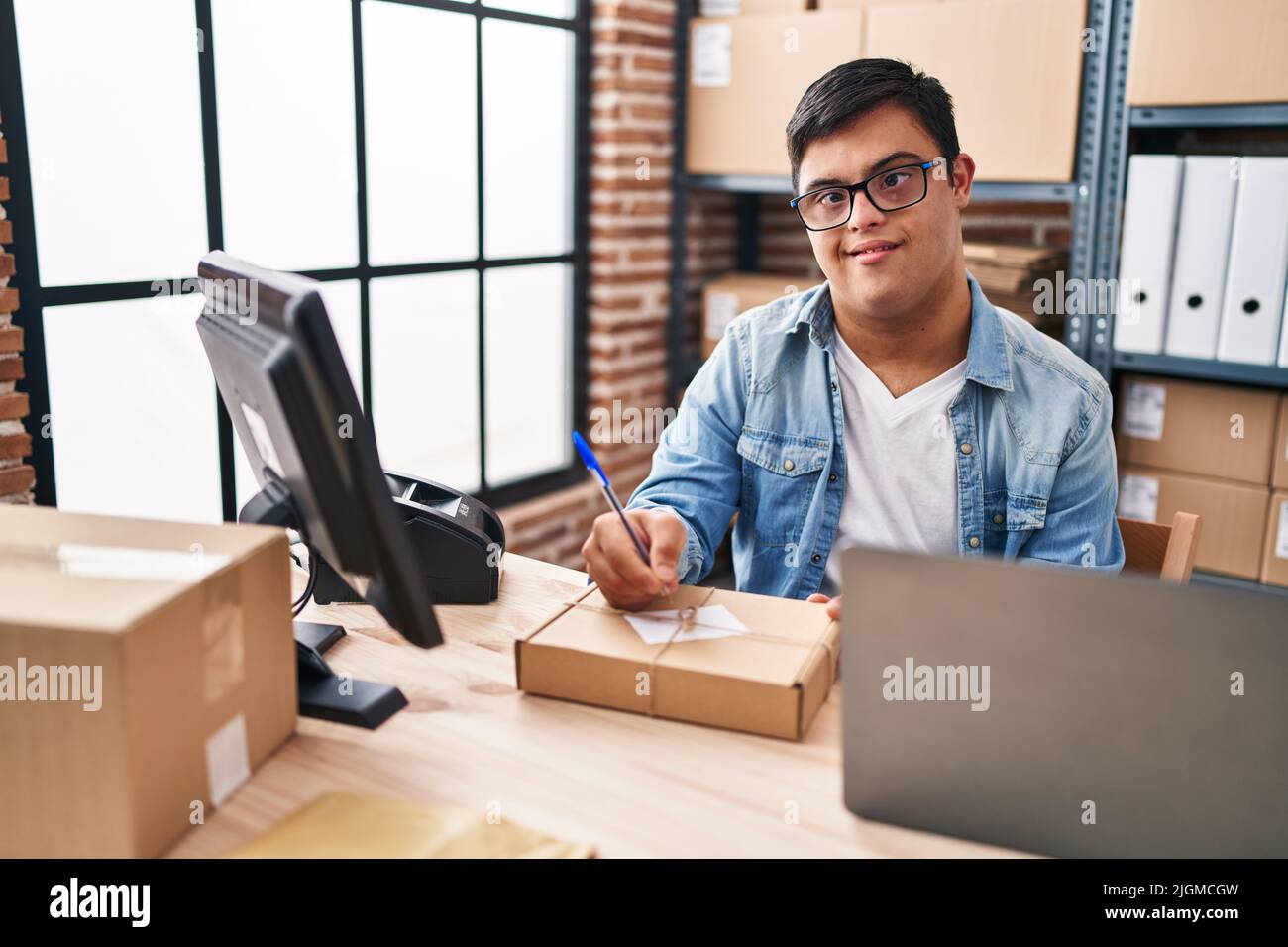 Down syndrome man ecommerce business worker writing on package at office Stock Photo