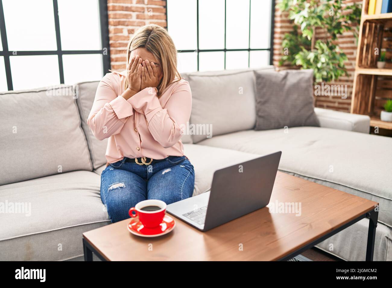 Young hispanic woman using laptop sitting on the sofa at home with sad ...