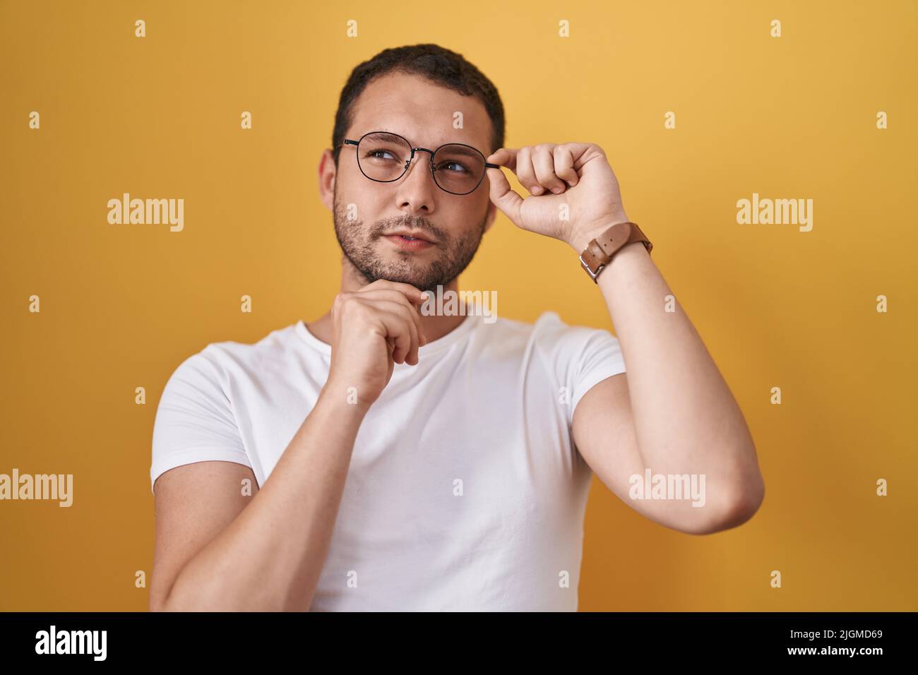 Hispanic man holding glasses serious face thinking about question with hand on chin, thoughtful about confusing idea Stock Photo
