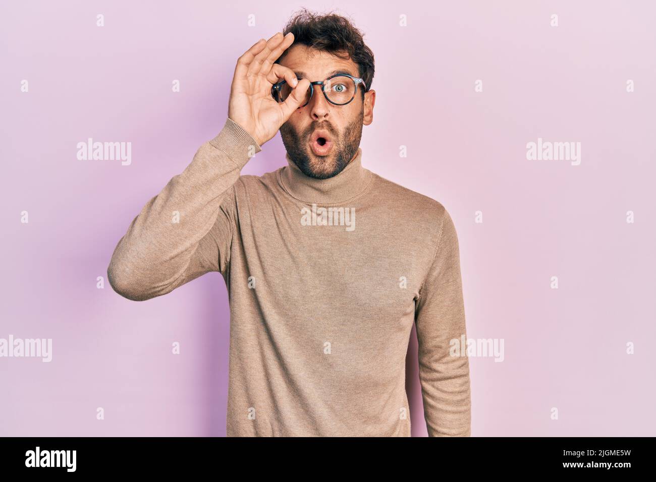 Handsome man with beard wearing turtleneck sweater and glasses doing ok  gesture shocked with surprised face, eye looking through fingers.  unbelieving Stock Photo - Alamy