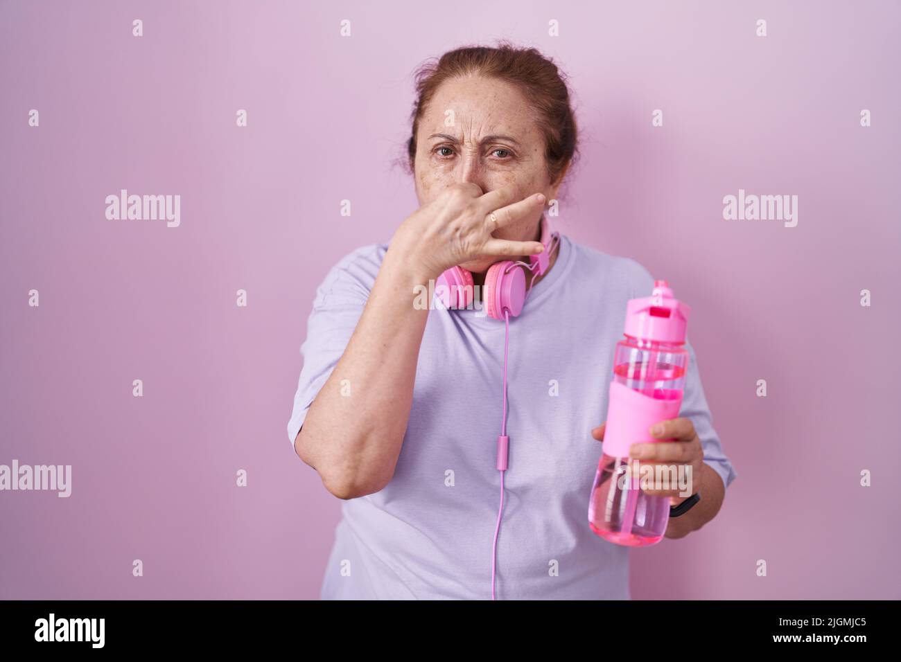 Senior woman wearing sportswear and headphones smelling something stinky and disgusting