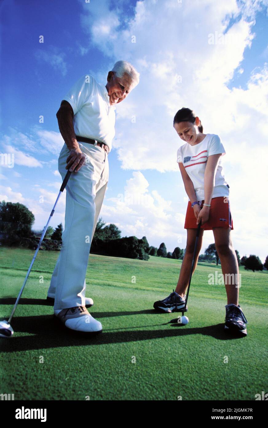 A grandfather teaches his grand daughter the basics of putting on the practice green. Stock Photo