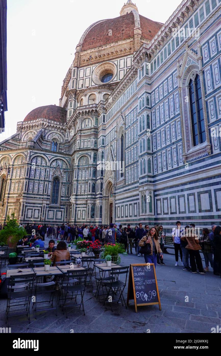 People in line, along the side of the great cathedral, waiting to enter the Duomo while others sit at outdoor restaurant tables, Florence, Italy. Stock Photo
