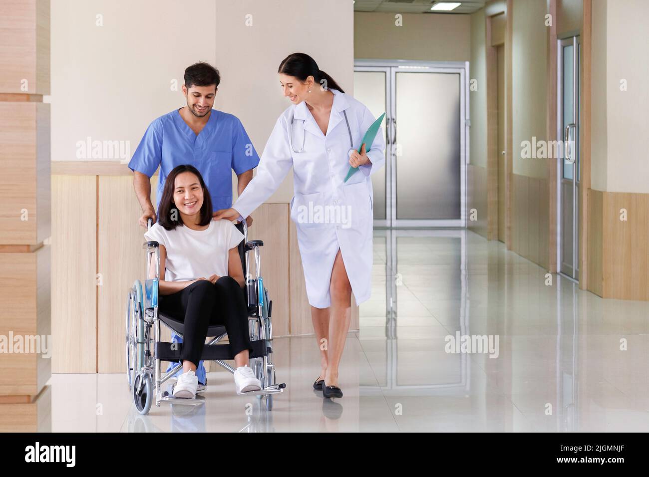 happy smiling asian patient woman sitting in wheelchair with male nurse talking to doctor after recovering from surgery treatment plan in the hospital Stock Photo