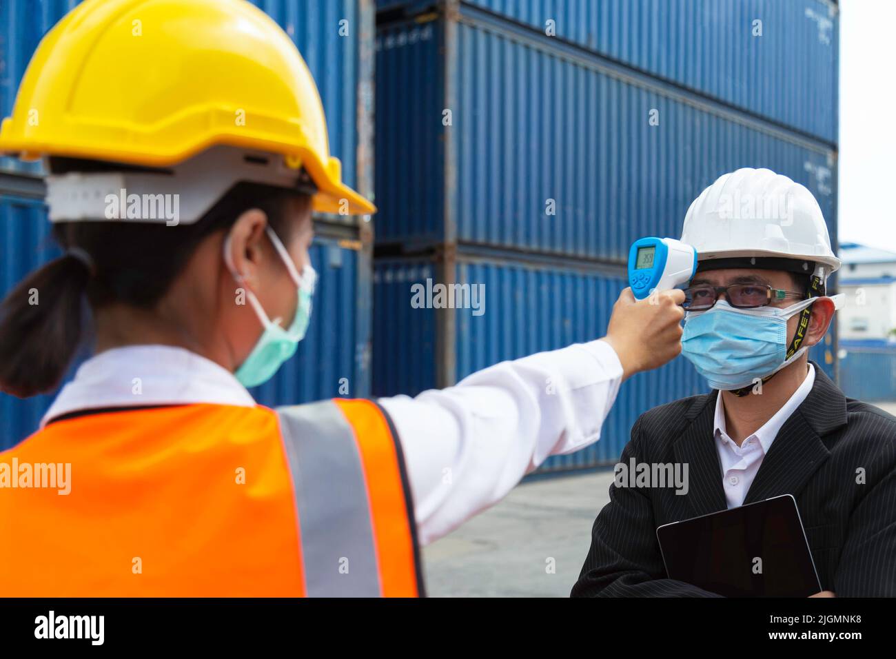 asian businessman wearing face mask checking fever by digital thermometer before entering work in logistic cargo warehouse at manufacturing  to protec Stock Photo