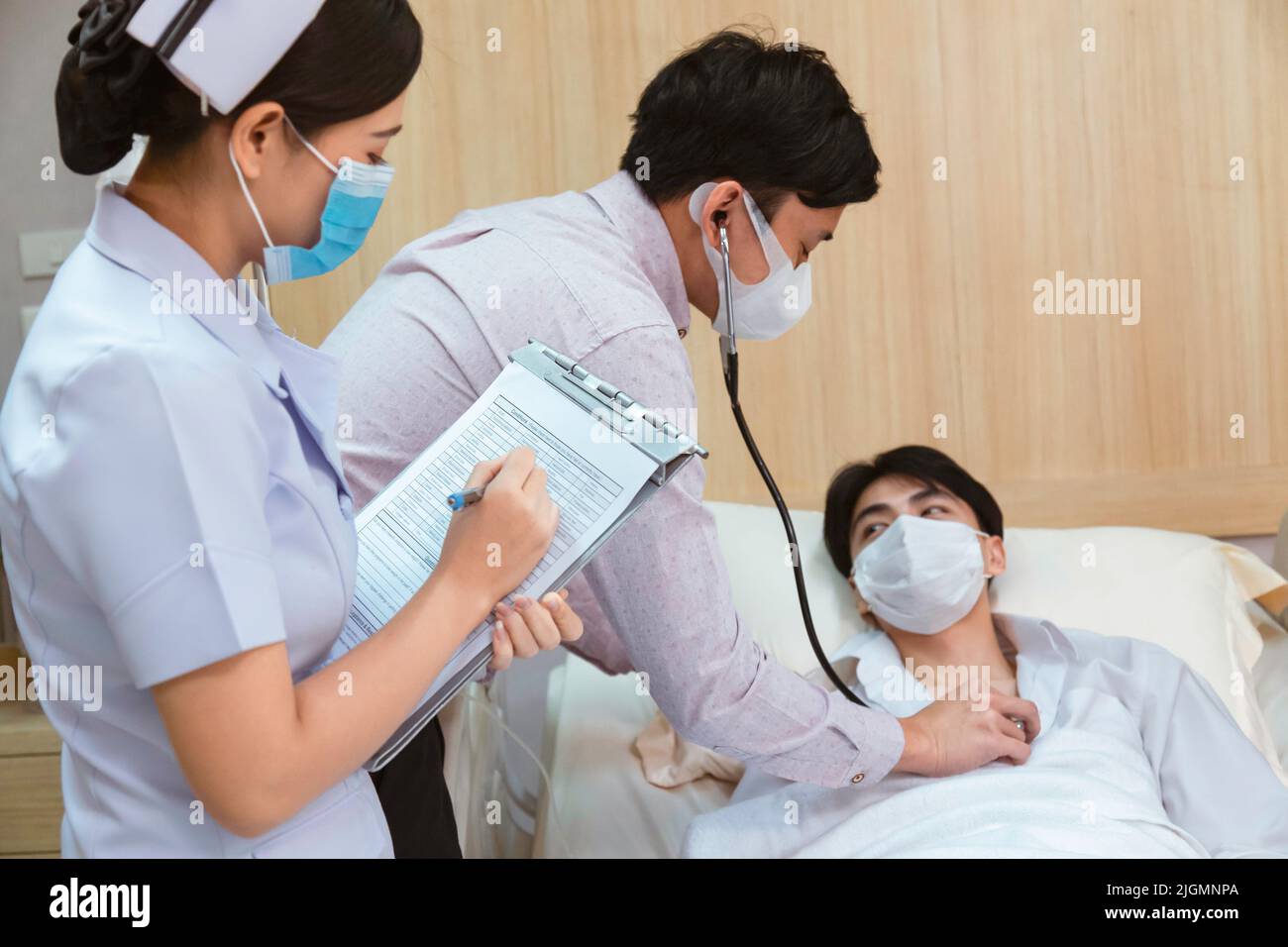 asian man patient lying in bed while doctor check heartbeat by stethoscope and woman nurse writing health checklist at the hospital. healthcare and ho Stock Photo