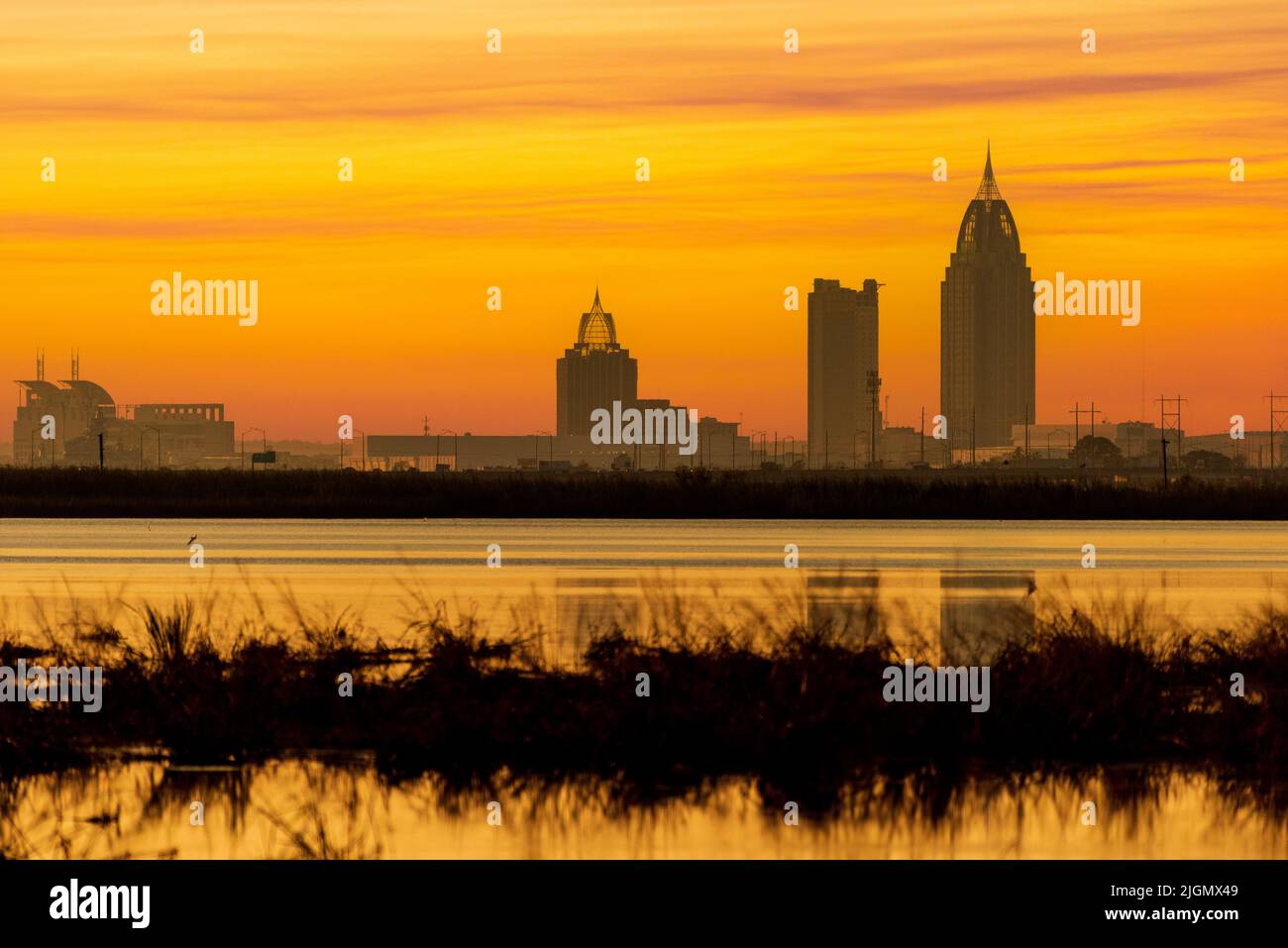 The setting sun paints the sky beyond the skyline of Mobile, Alabama, as seen from across Mobile Bay in a composite image. Stock Photo