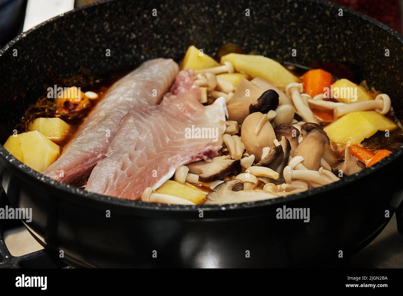 Fish stewed with carrots, mushrooms and potatoes is fried in pan on gas