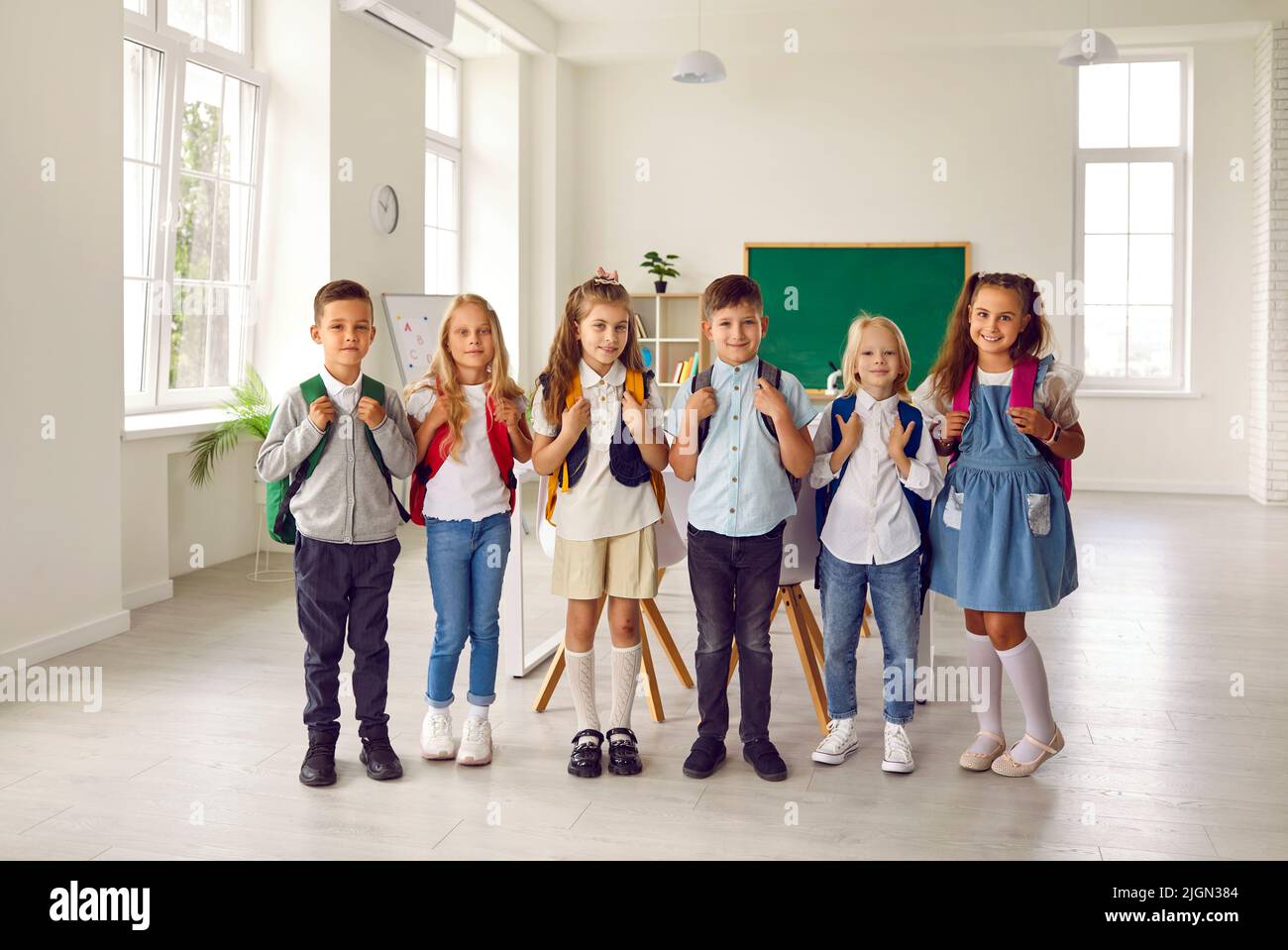 Portrait of small smiling group of first graders in modern elementary school classroom. Stock Photo