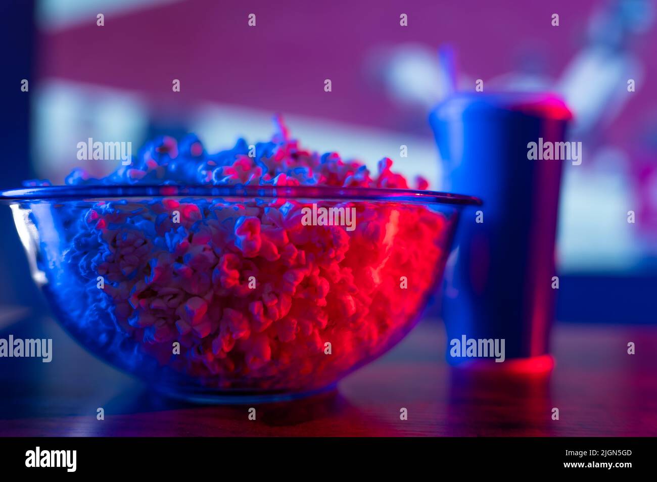 Close-up. A large glass bowl with popcorn and a drink in a glass on a wooden table. Comfort and homeliness. Watch your favorite movies, series, music Stock Photo