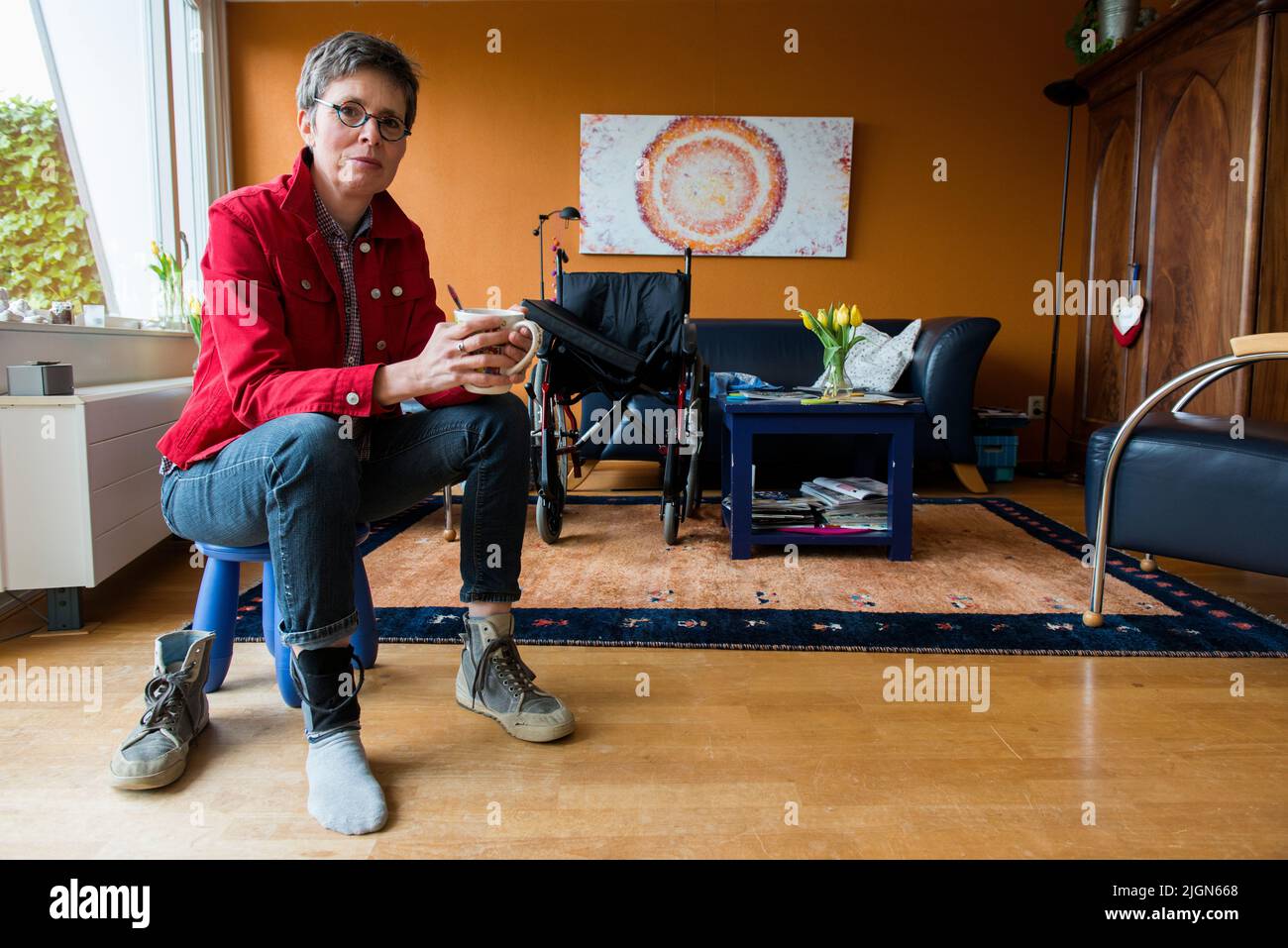 Tilburg, Netherlands. Living room portrait of a mature adult woman suffering from Multiple Sclerosis sitting besides her wheelchair. Stock Photo