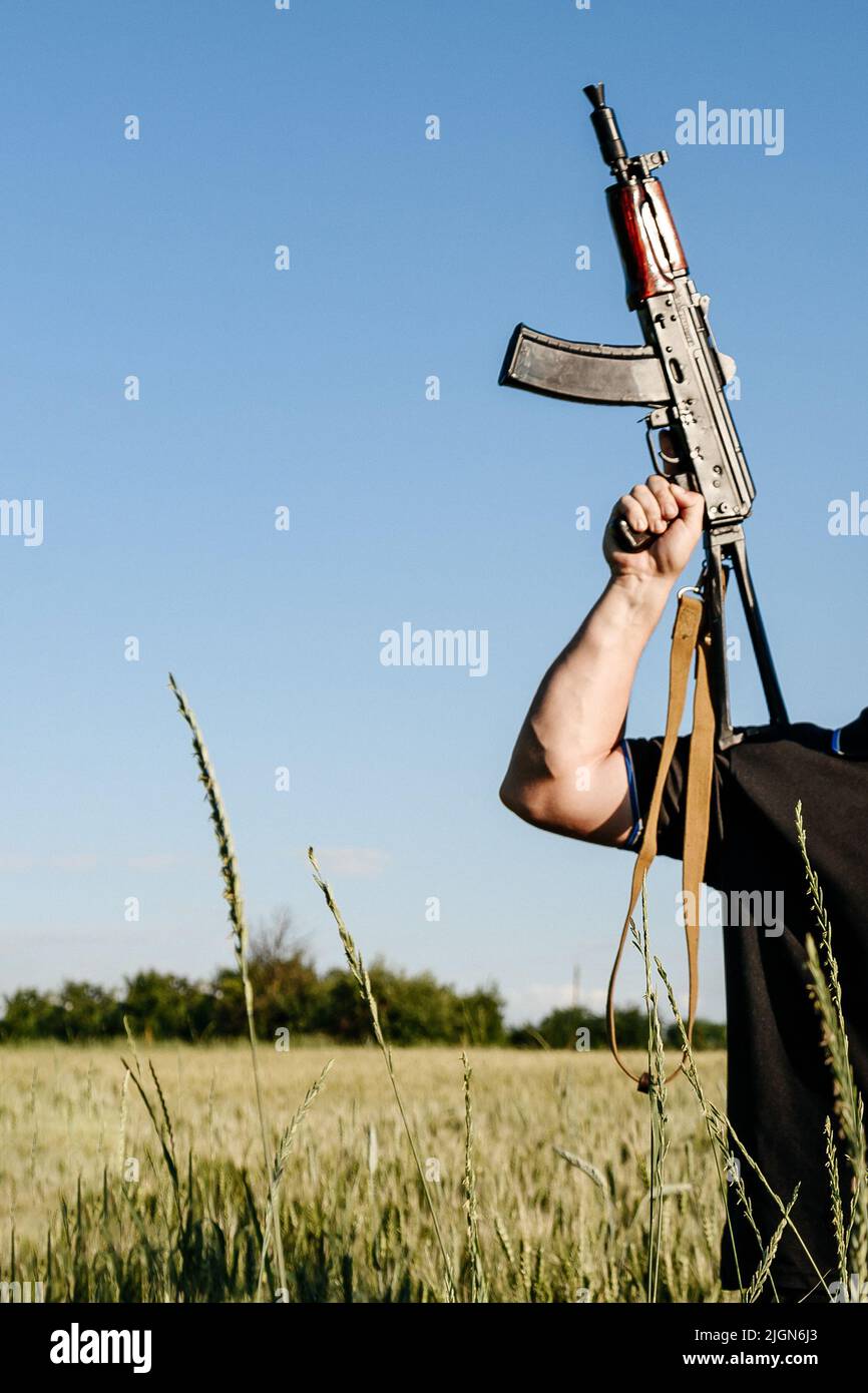 A soldier with a combat military assault rifles AK 74 stands in a field, Ukrainian wheat fields and war, guerrilla movement in ukraine, guerrilla sold Stock Photo