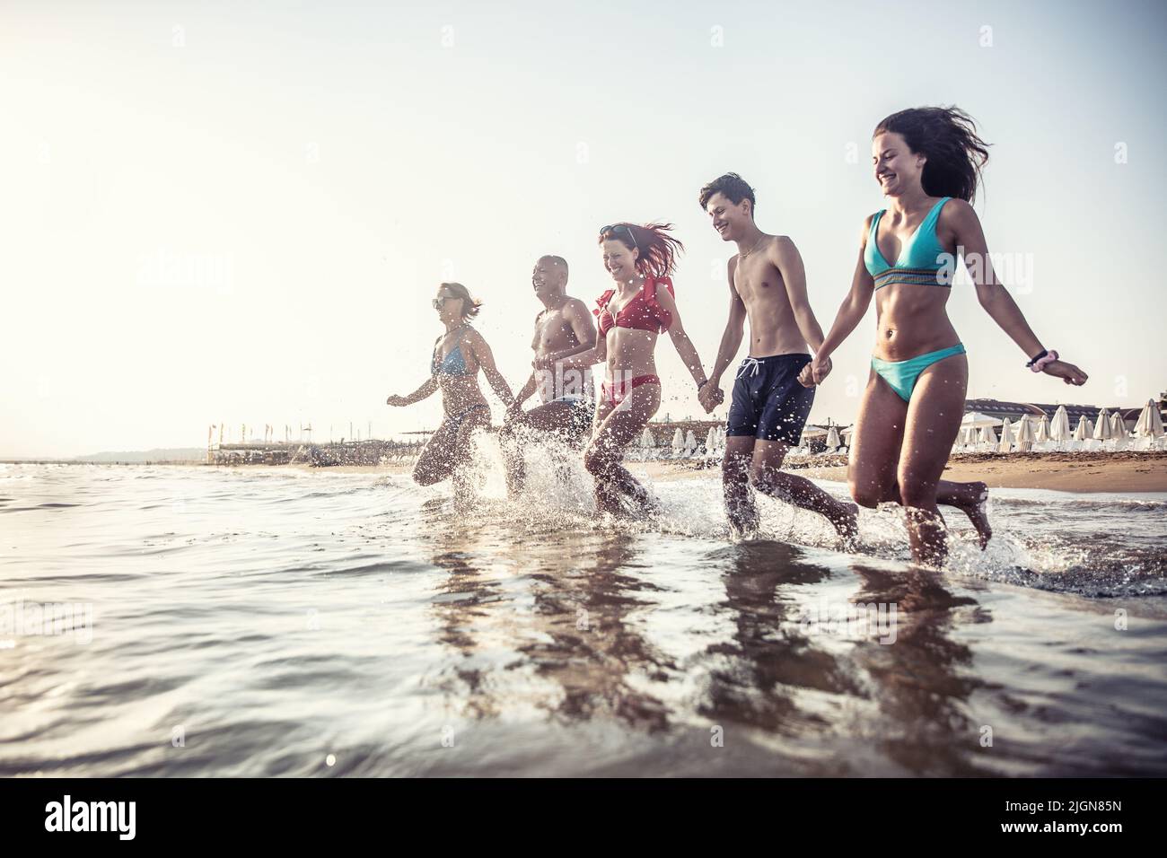 The complete family runs hand in hand from the beach to the sea, enjoying a joint vacation by the sea. Stock Photo