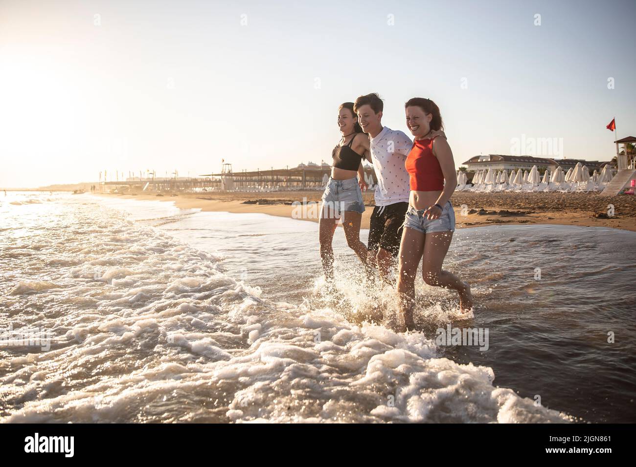 Three siblings enjoy their vacation by the sea and run into the sea at sunset. Stock Photo