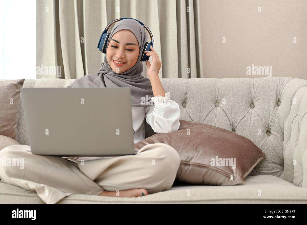 Pretty charming young Asian Muslim woman wearing hijab and headphones ...