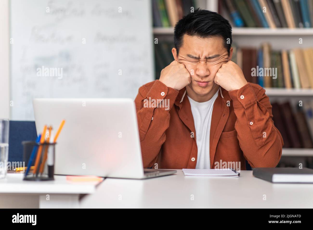 Tired Asian Teacher Sitting With Eyes Closed Near Laptop Indoor Stock Photo