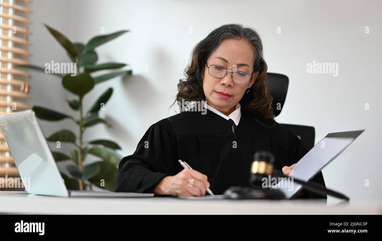 Experienced mature female lawyer using laptop and preparing contract or document for courtroom legal Stock Photo