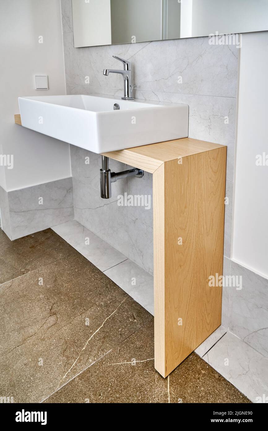 Modern ceramic sink with faucet installed on wooden console table in bathroom. Sanitary engineering with stylish design for bathroom interior Stock Photo