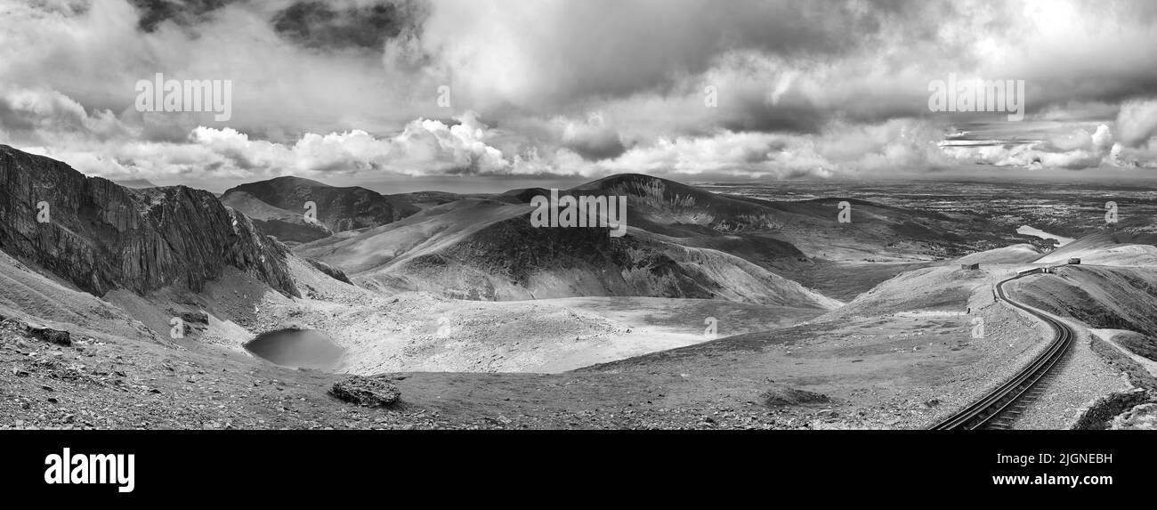 Panorama of the mountains of Snowdonia looking from Mount Snowdon, with a vintage steam train climbing from the town of LLanberis to the summit. Black Stock Photo