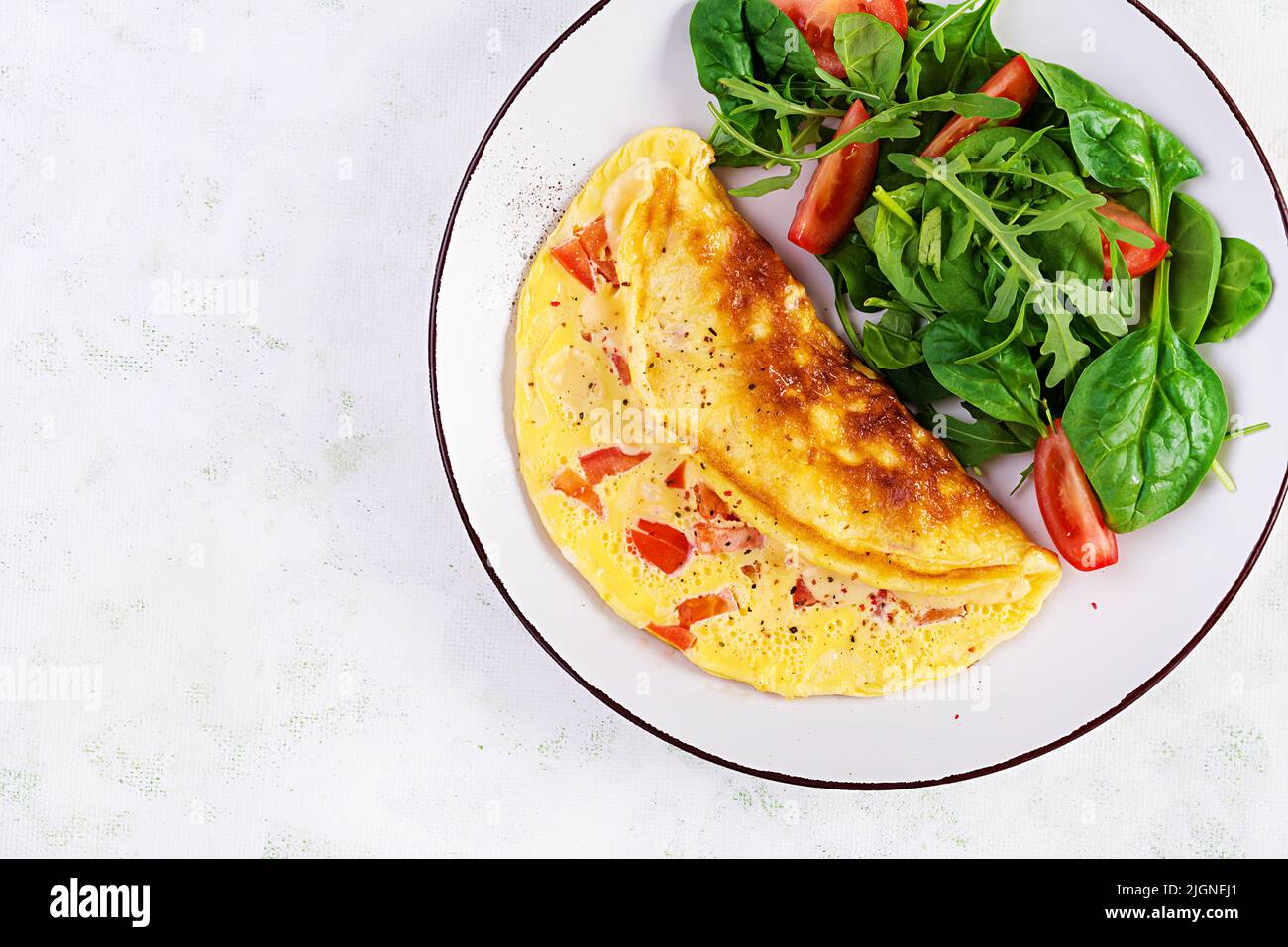 Omelette with tomatoes and salad on white plate.  Frittata - italian omelet. Top view Stock Photo