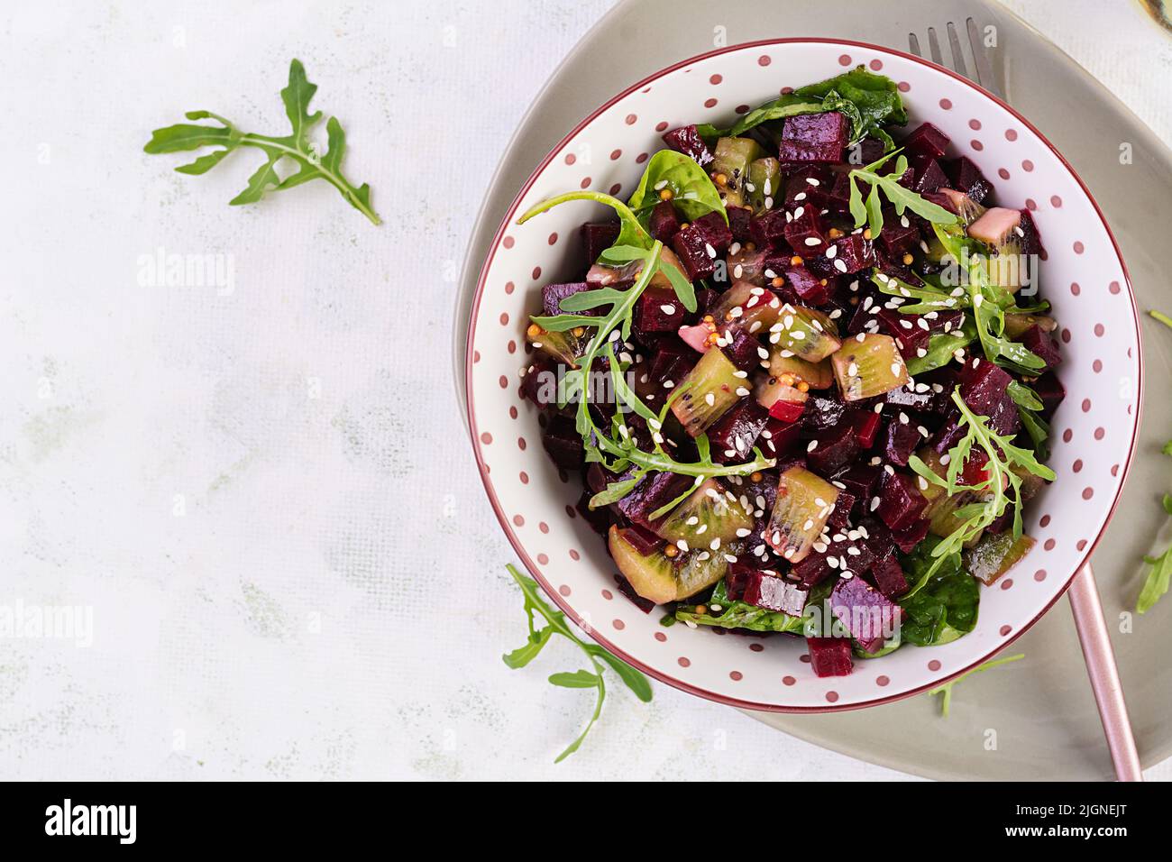 Bowl with salad with baked beetroots, kiwi, spinach, arugula and dressing mustard, oil. Top view, flat lay Stock Photo