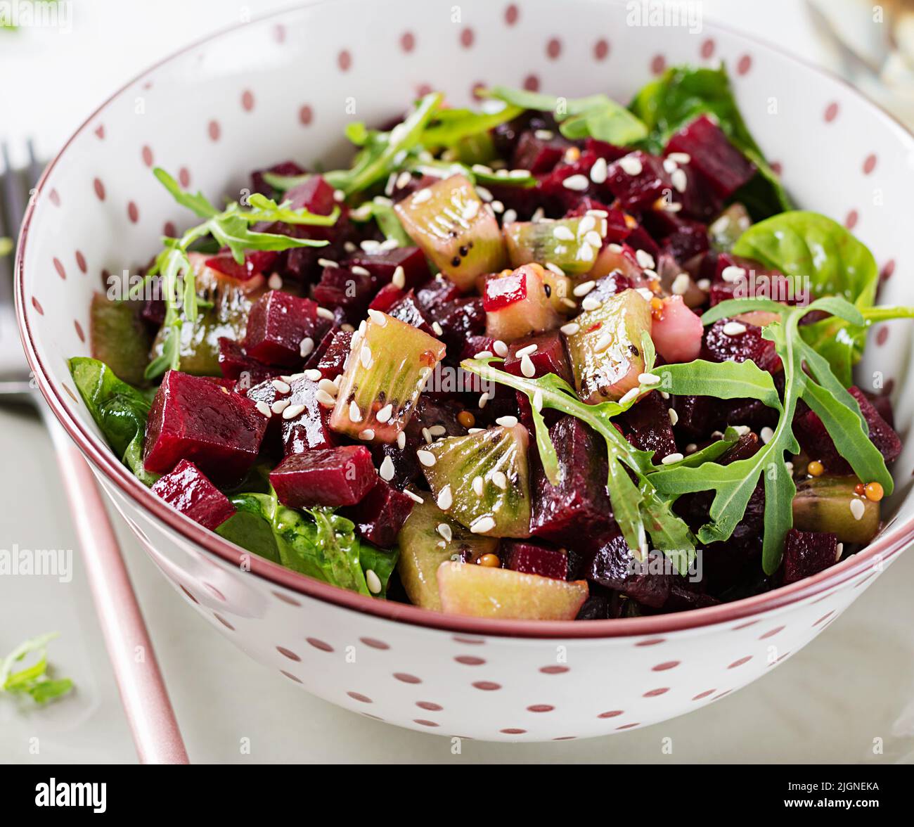 Bowl with salad with baked beetroots, kiwi, spinach, arugula and dressing mustard, oil. Stock Photo