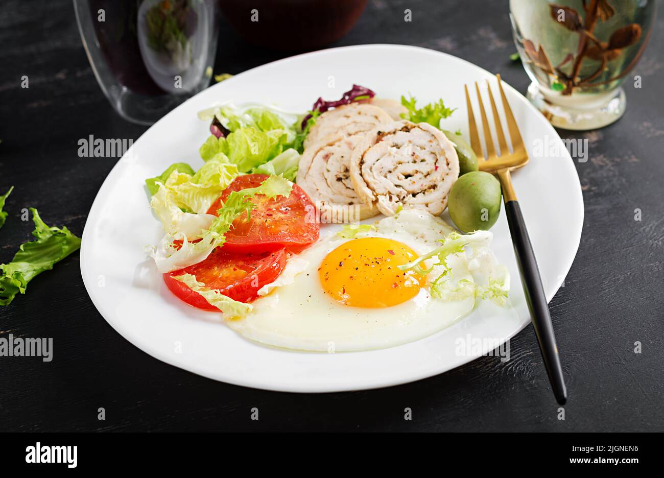 Fried egg, meat chicken roll, olives and tomatoes. Keto, paleo breakfast. Ketogenic food. Stock Photo