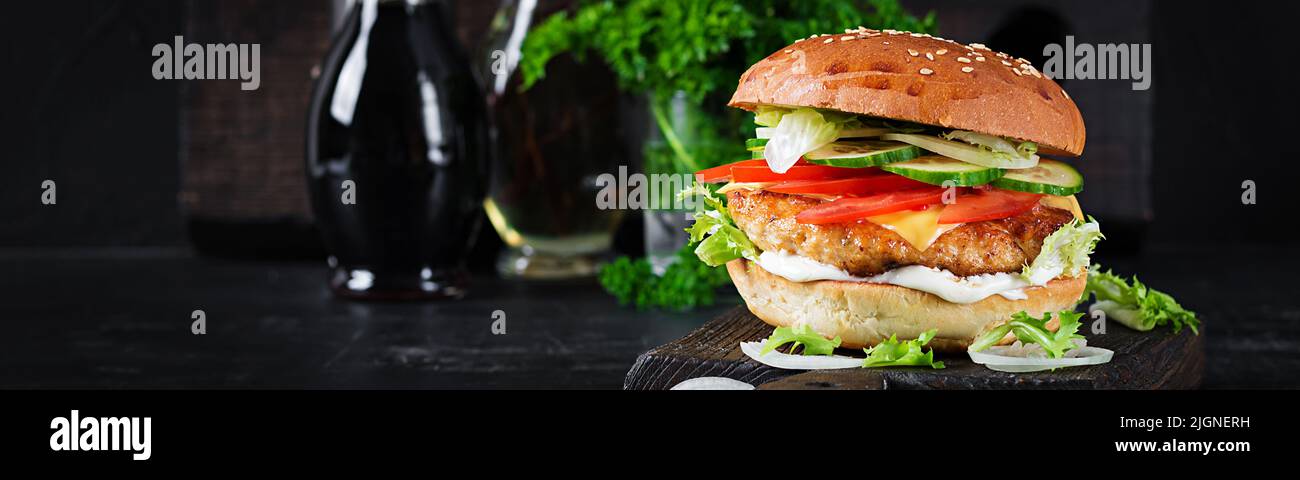 Hamburger with chicken burger meat, cheese, tomato, cucumber and lettuce on wooden background. Tasty burger. Banner. Close up Stock Photo