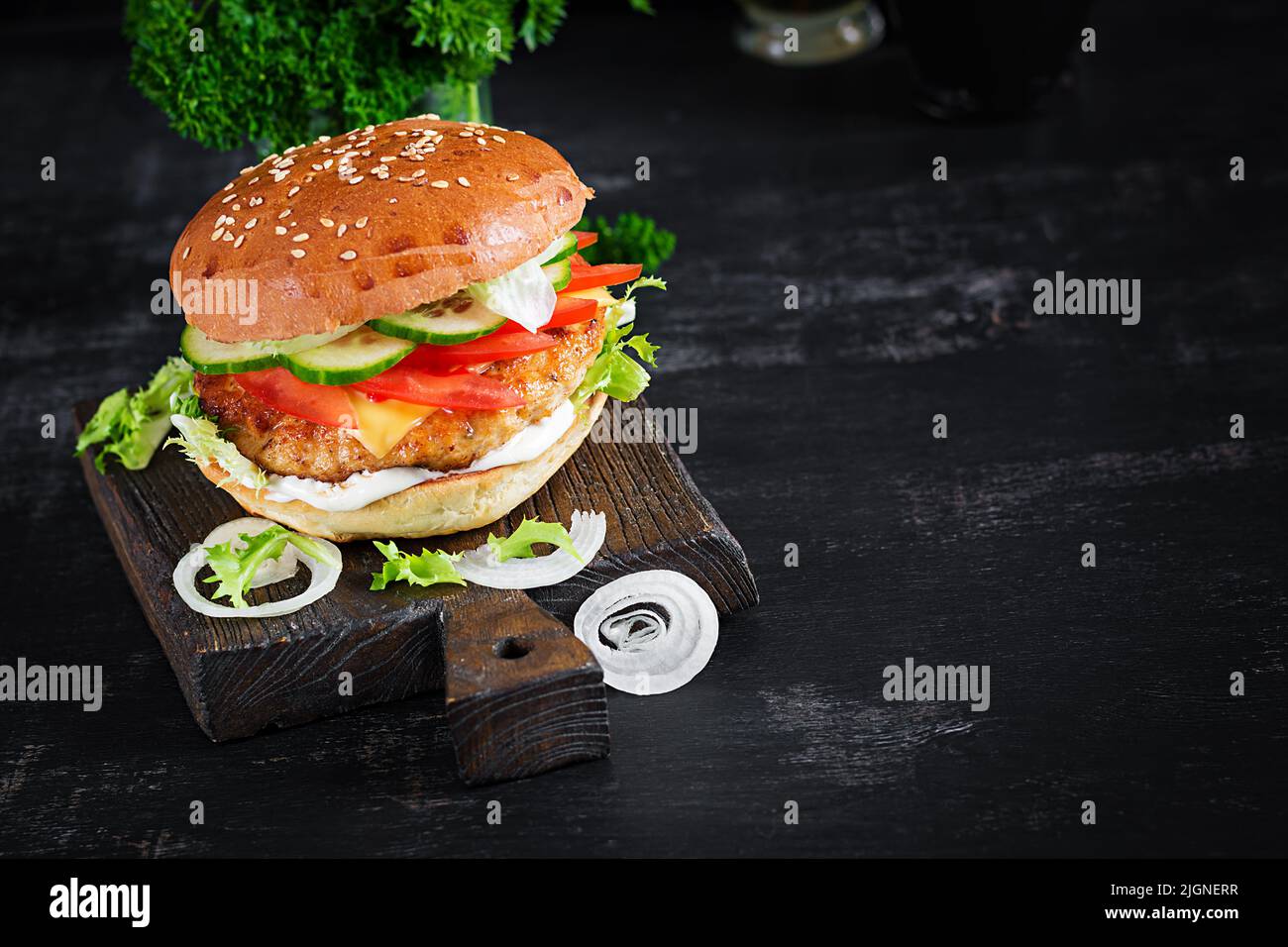 Hamburger with chicken burger meat, cheese, tomato, cucumber and lettuce on wooden background. Tasty burger. Close up Stock Photo