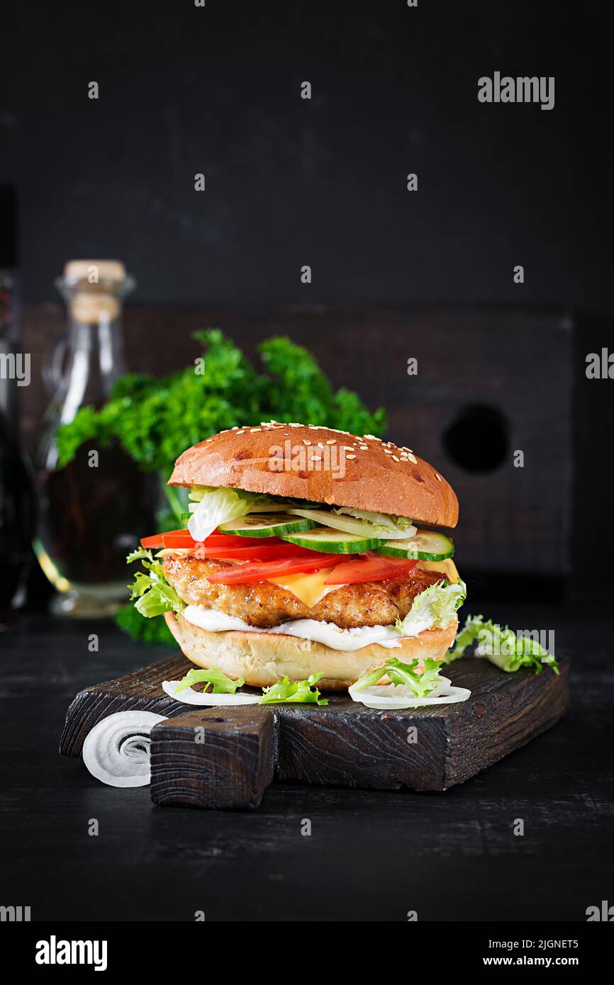 Hamburger with chicken burger meat, cheese, tomato, cucumber and lettuce on wooden background. Tasty burger. Close up Stock Photo