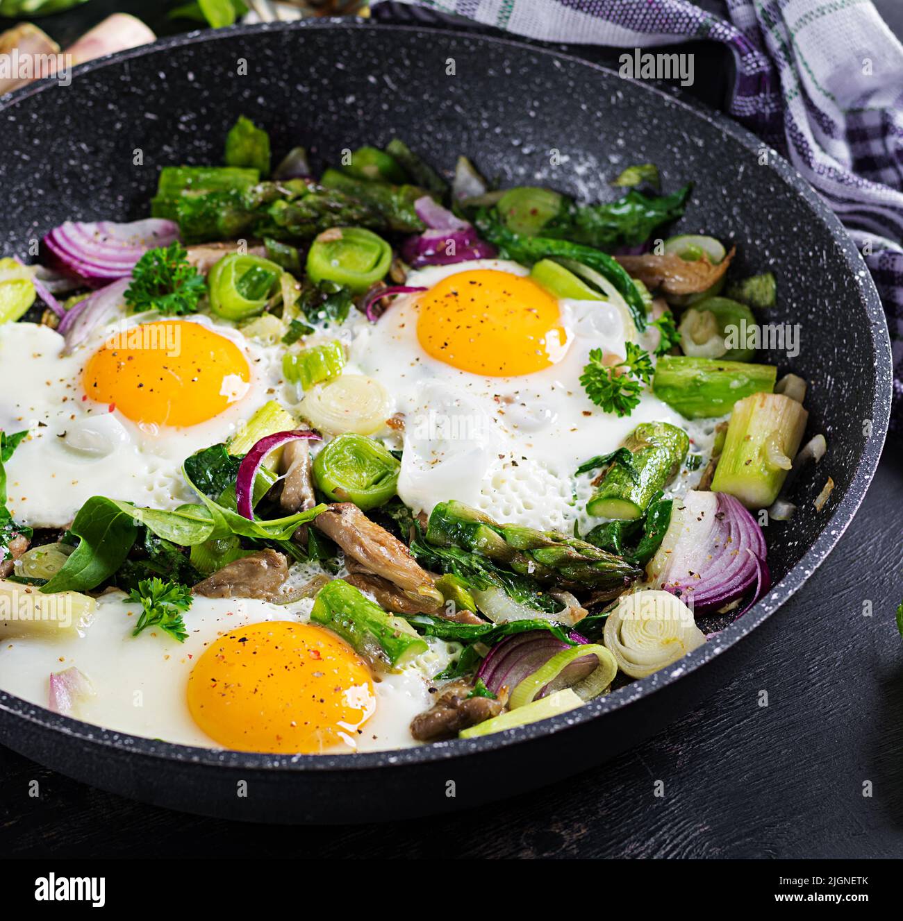 Fried eggs with asparagus, leeks, spinach and mushrooms. Useful breakfast. Stock Photo