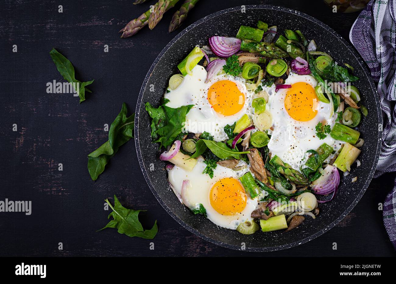 Fried eggs with asparagus, leeks, spinach and mushrooms. Useful breakfast. Top view, overhead Stock Photo