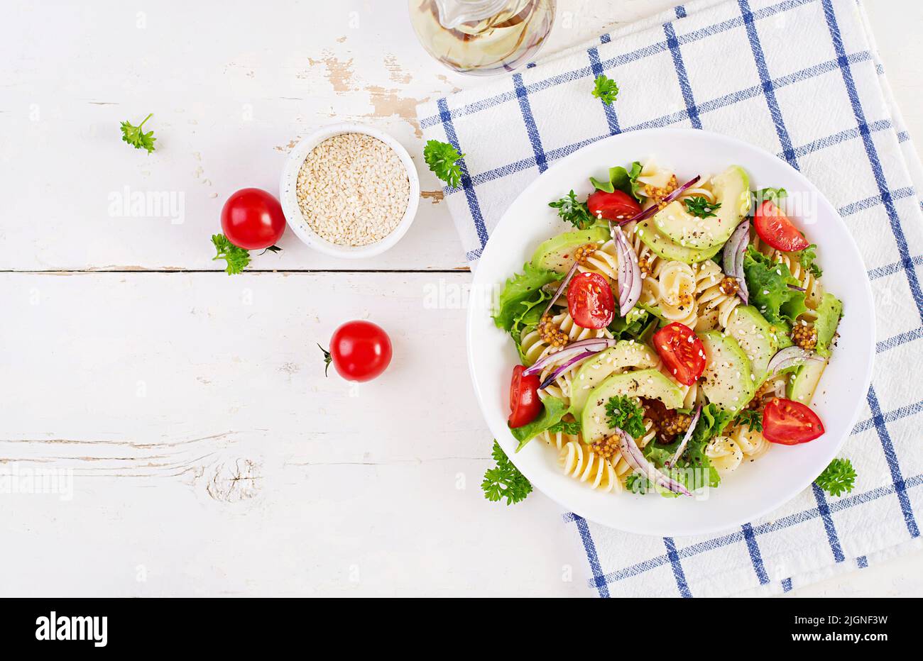 Fusilli pasta salad with avocado, tomatoes, fresh green lettuce, red onion and mustard dressing on white background. Vegetarian healthy lunch. Top vie Stock Photo