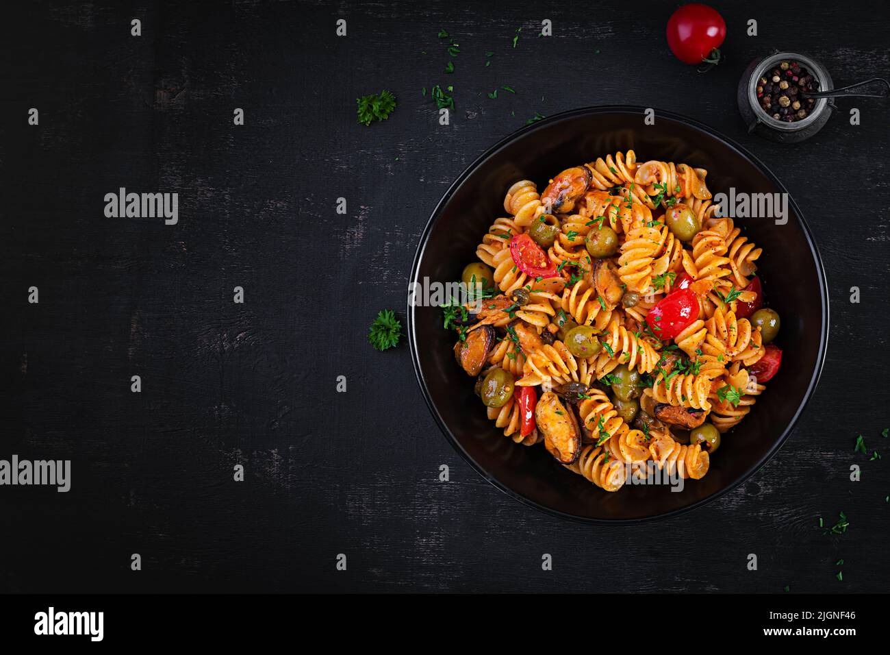 Classic italian pasta fusilli marinara with mussels, green olives and capers on dark table.  Fusilli pasta with sauce marinara. Top view, overhead Stock Photo