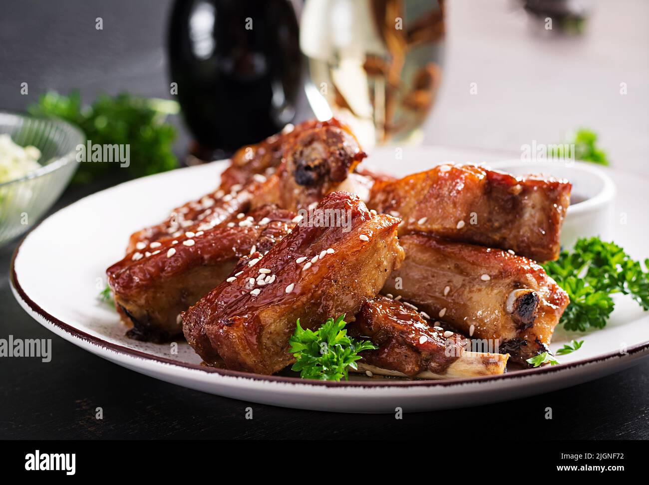 Delicious barbecued spare ribs on plate on dark background. Tasty bbq meat. Stock Photo
