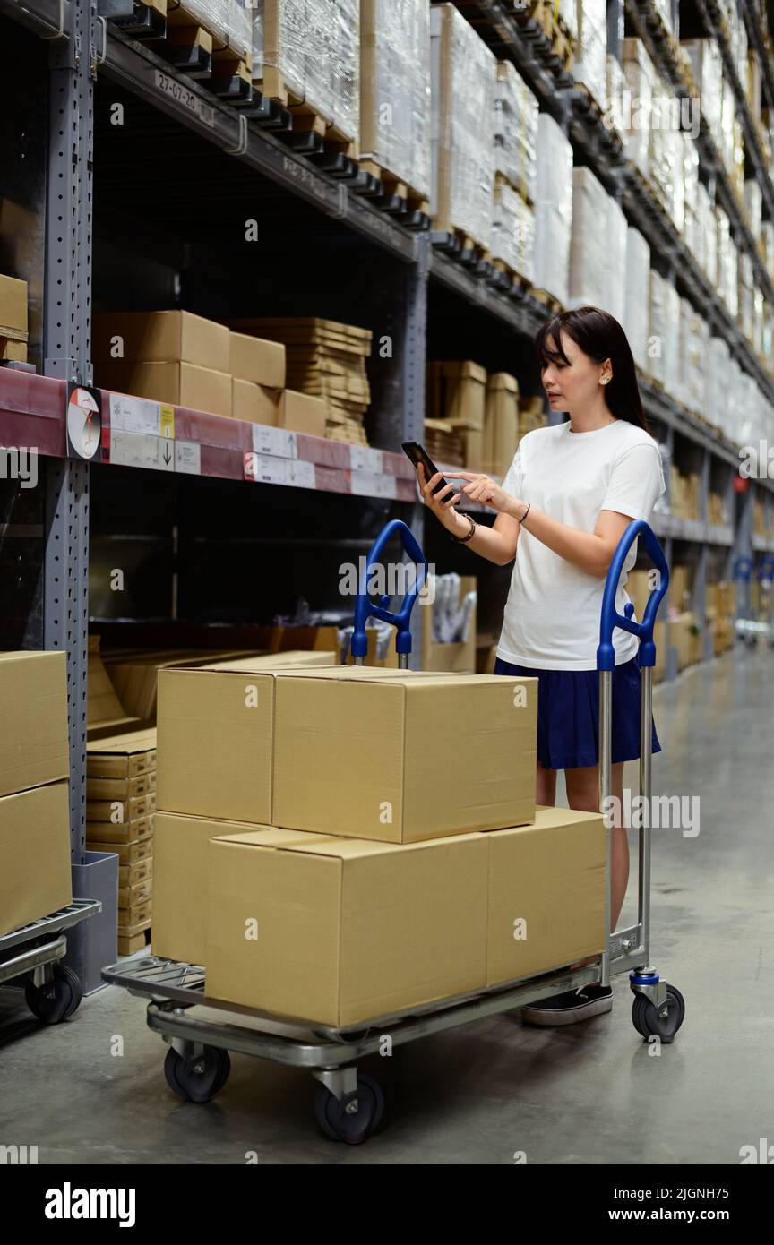 Portrait of asian woman using smartphone checking products in a furniture warehouse Stock Photo