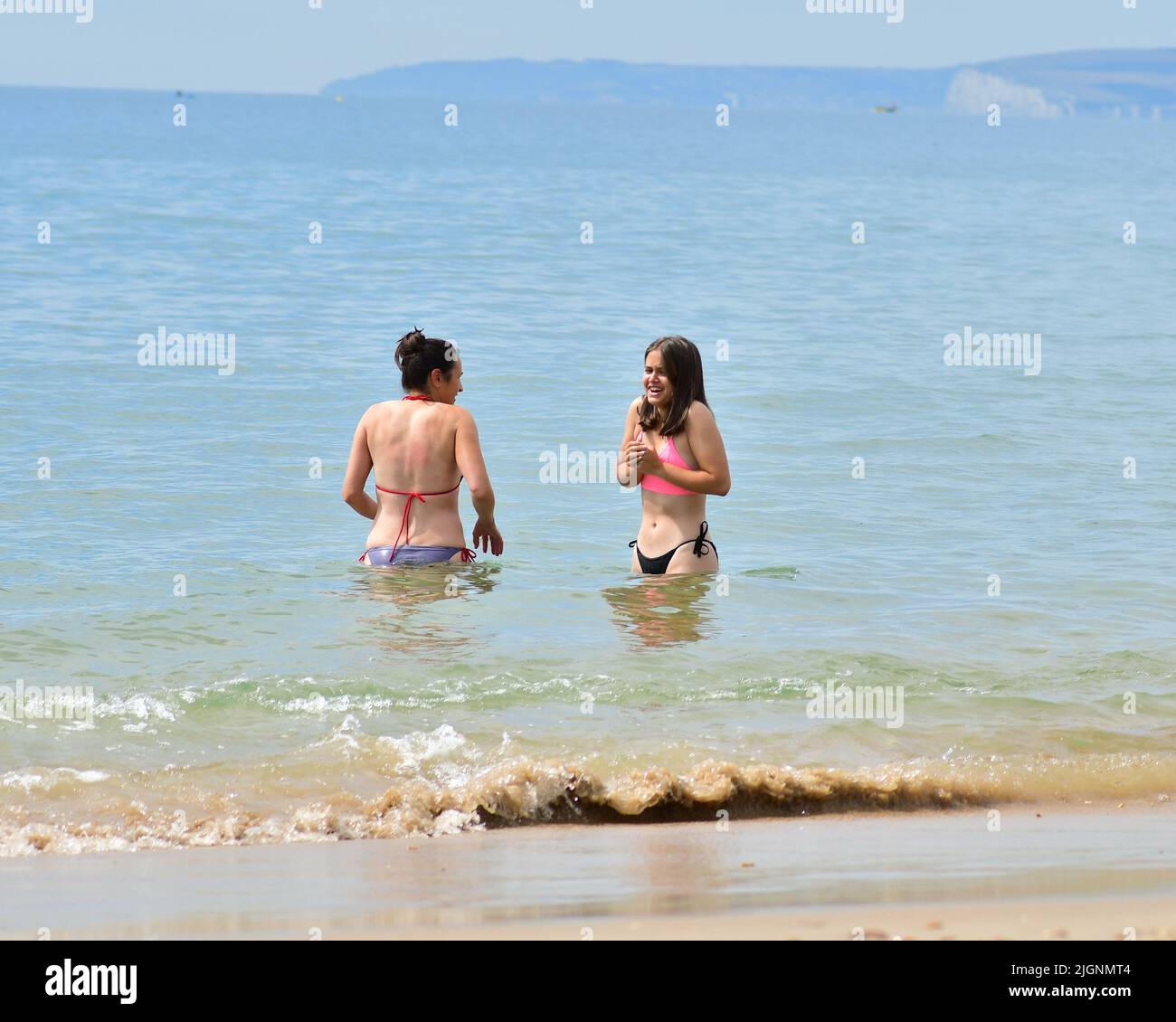 Boscombe, Bournemouth, Dorset, England, UK, 12th July 2022, Weather. Long heatwave in mid-summer. People are on the beach in the morning. Two women in bikinis venture into the cool sea. Credit: Paul Biggins/Alamy Live News Stock Photo