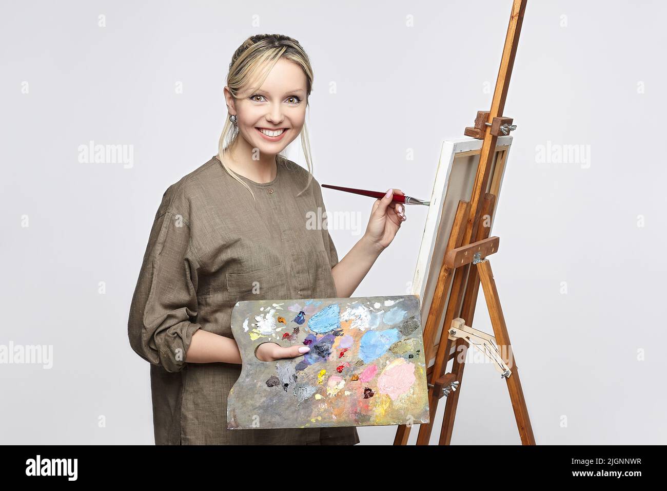 young artist poses with a palette and brush in front of an easel in the ...