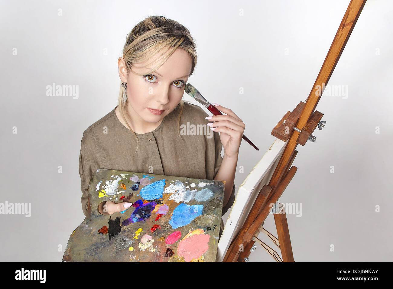 young artist poses with a palette and brush in front of an easel in the ...
