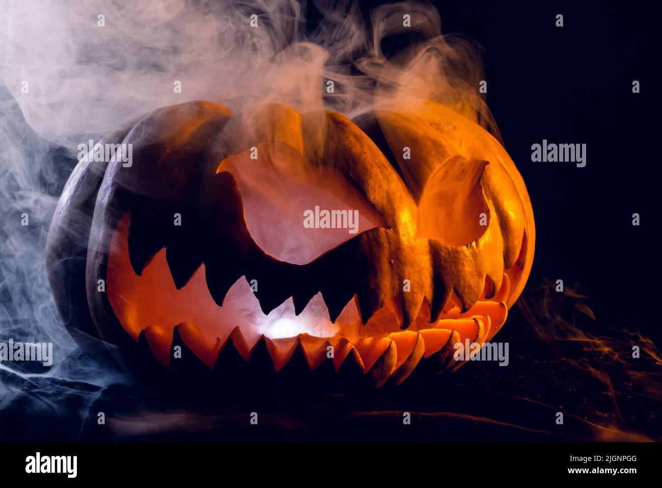 Composition of halloween carved pumpkin with smoke and orange light on